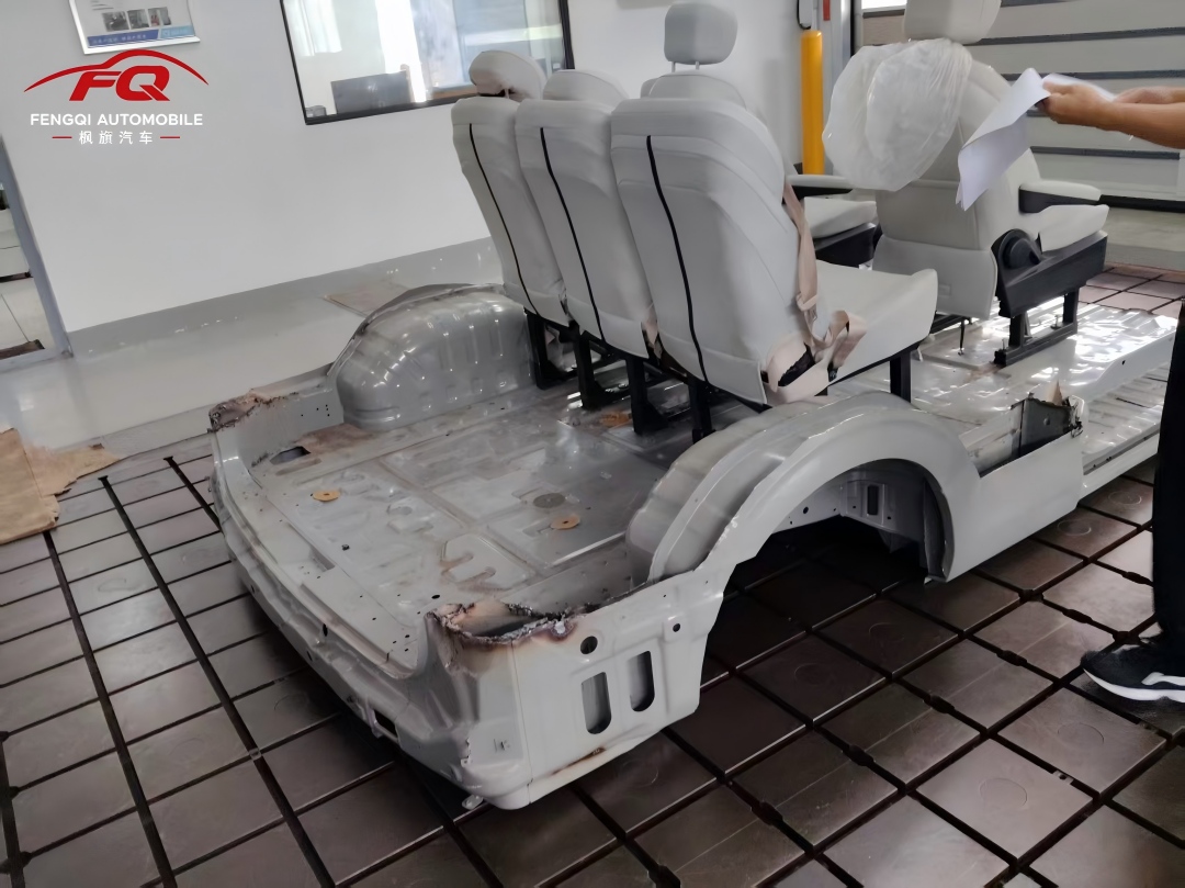 A bare white vehicle body on a test platform with seats bolted directly to it — the seat anchorage and belt-anchor strength test for the F150 command vehicle.